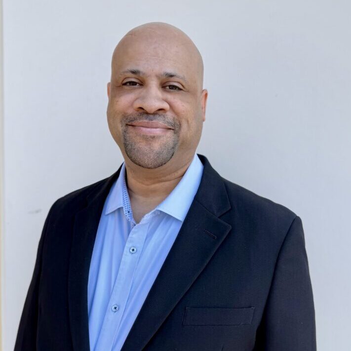 Mike Roberts, Founder and CEO of Creating Coding Careers, smiling in a casual black polo shirt against a neutral background, embodying leadership and commitment to diversity in tech.