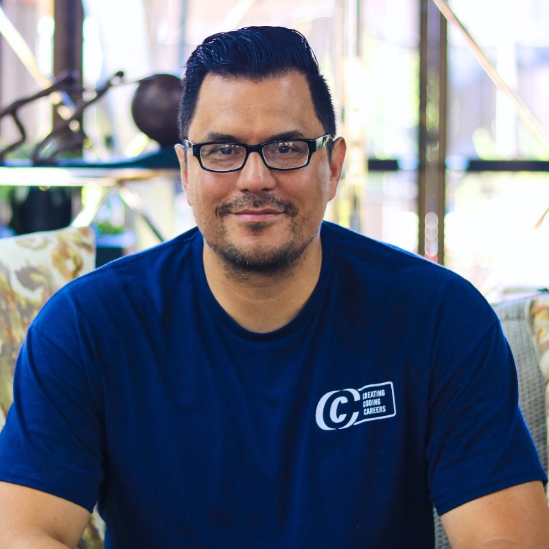 Instructor from Creating Coding Careers wearing a navy polo shirt with the organization's logo, smiling in a professional setting.